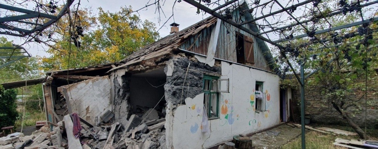 Пошкоджений приватний будинок із частково зруйнованими стінами та дахом. На фасаді – дитячі малюнки, поруч уламки цегли та деревини.