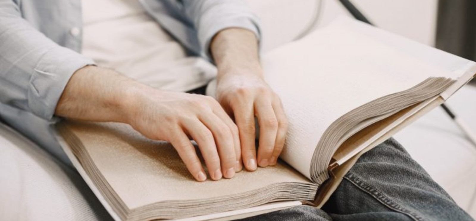 Людина читає книгу, надруковану шрифтом Брайля, проводячи пальцями по рельєфних сторінках.