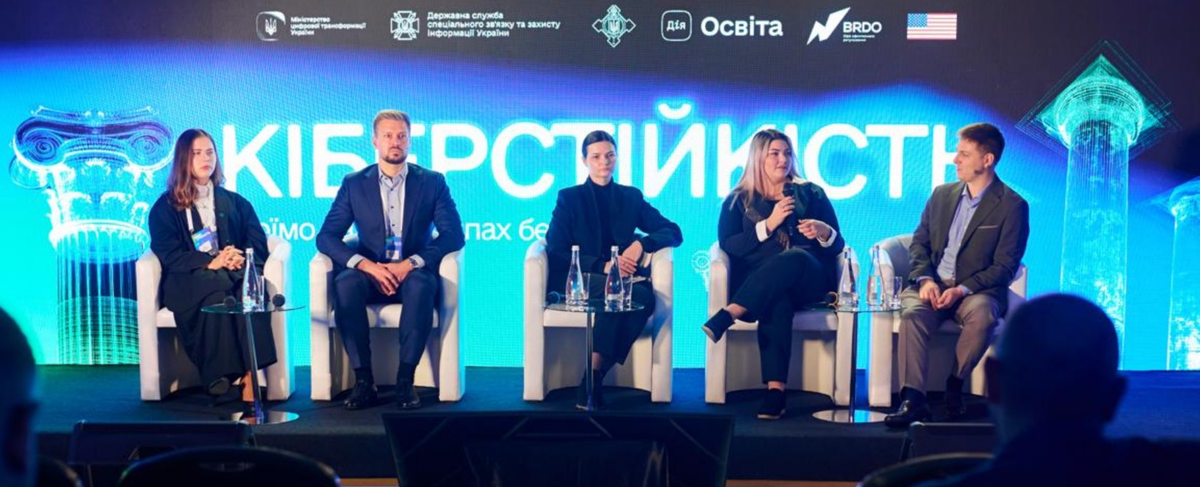 Учасники презентації обговорюють питання цифрової безпеки. На екрані позаду — великий надпис «Кіберстійкість» та логотипи організаторів заходу, зокрема Міністерства цифрової трансформації України та партнерів.