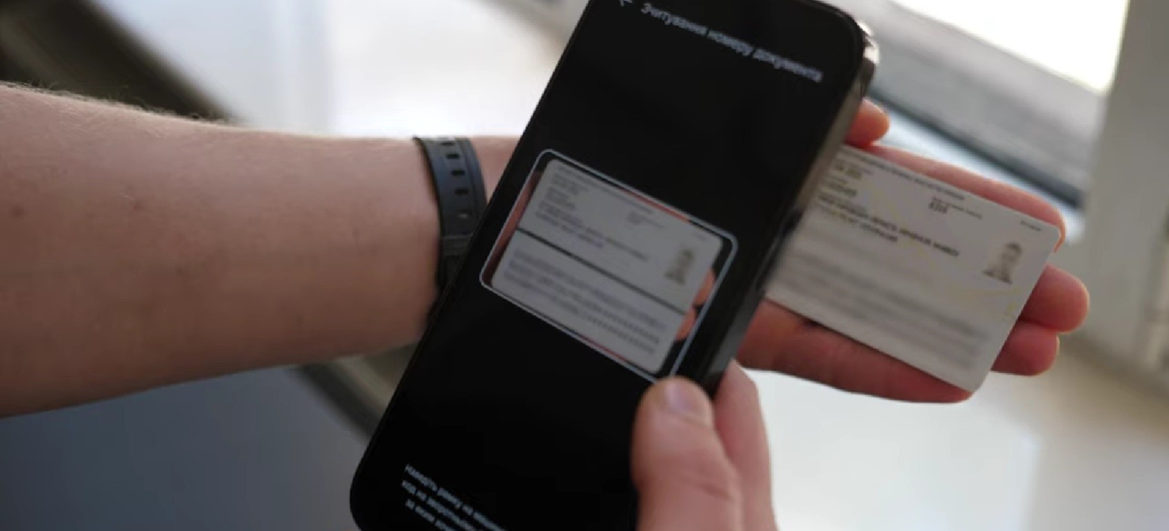 Людина тримає смартфон і пластикову ID-картку, скануючи документ через додаток для авторизації в “Дії”.