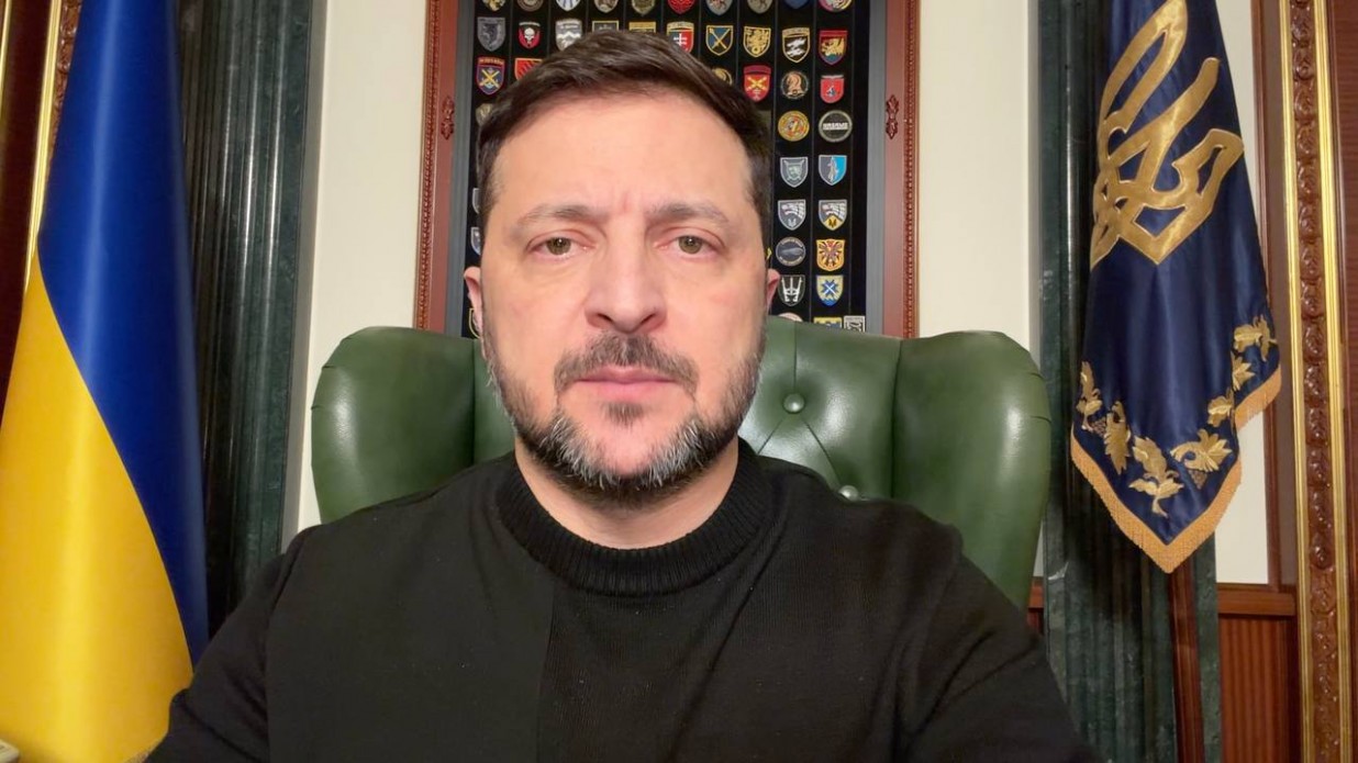 Чоловік середнього віку з короткою бородою, одягнений у чорний джемпер, звертається на камеру на фоні офіційного кабінету.