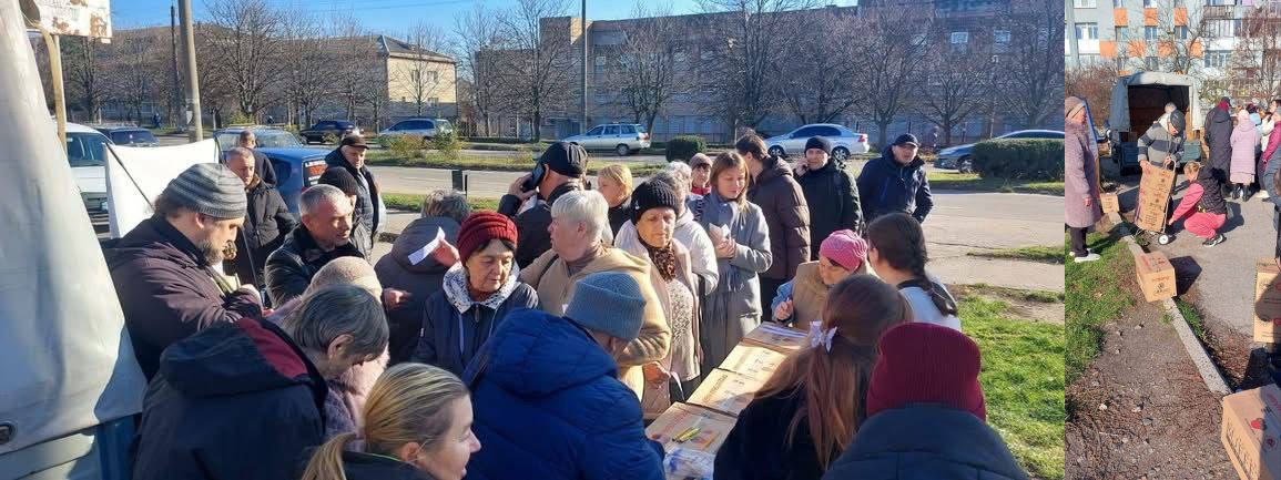 Велика група людей, які стоять на вулиці та отримують гуманітарну допомогу, ймовірно, у міському районі. На задньому плані видно автомобілі та житлові будинки.