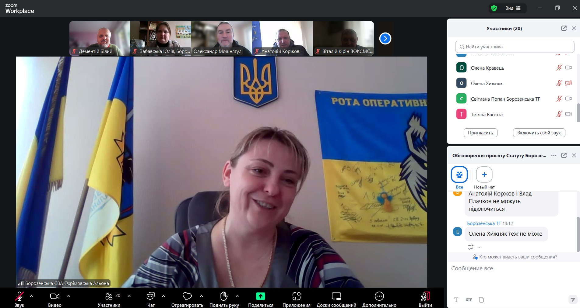 Скриншот онлайн-наради в Zoom. У центрі — велике відеовікно з жінкою на фоні державних прапорів України та герба. Зверху розташована стрічка з мініатюрами інших учасників, а праворуч — бічні панелі зі списком присутніх та активним чатом.