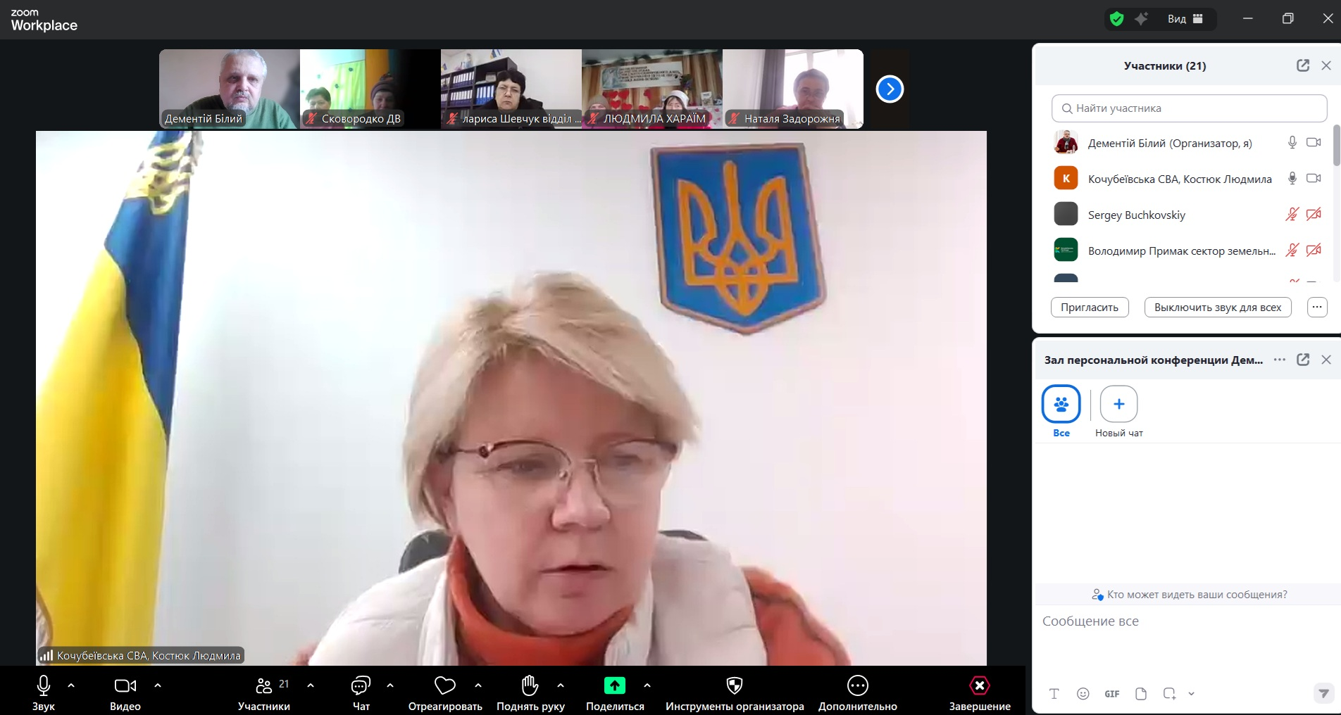 Скриншот онлайн-наради в Zoom. У центрі — велике вікно з жінкою в окулярах на фоні державного прапора України та синього щита з гербом. Зверху розташована стрічка з мініатюрами п'яти інших учасників, а праворуч — бічні панелі зі списком присутніх (21 особа) та вікном чату.