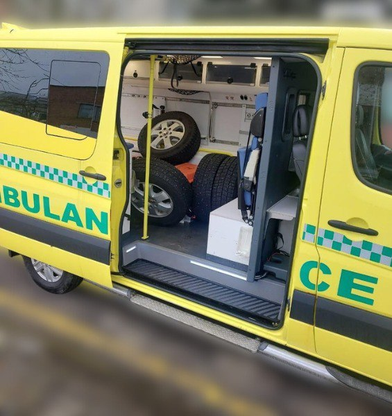 Жовтий автомобіль швидкої допомоги з написом «AMBULANCE», у салоні якого замість медичного обладнання складено декілька автомобільних коліс із шинами.