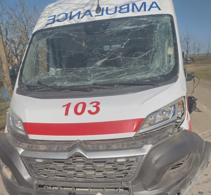 Автомобіль швидкої допомоги марки Citroen із серйозними пошкодженнями передньої частини. Лобове скло повністю розбите сіткою тріщин, бампер відірваний, а ліва фара та кузов пошкоджені. На капоті видно номер «103» та червону смугу.