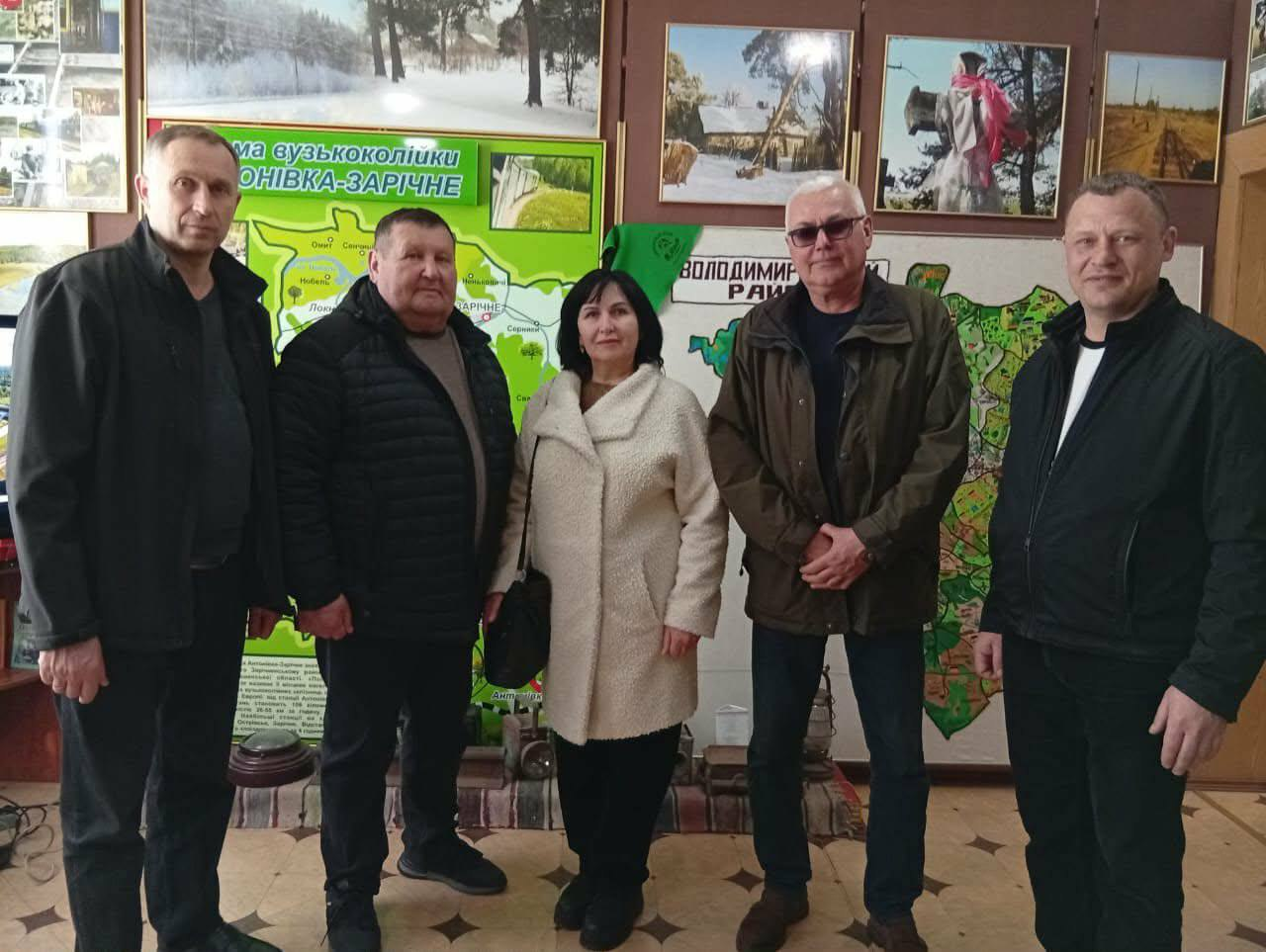 П'ятеро людей стоять у приміщенні на фоні інформаційних стендів. Ліворуч розміщена карта вузькоколійної залізниці «Антонівка-Зарічне», а праворуч — карта з написом «Володимирецький район». На стіні висять фотографії з краєвидами.