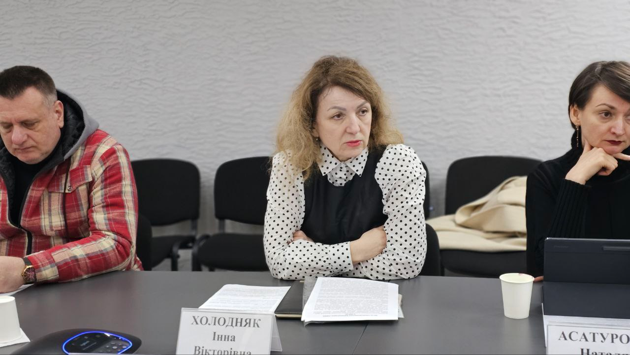 Представники влади та громадськості під час робочої зустрічі. Учасники сидять за столом із документами, планшетом та пристроєм для зв'язку; перед ними встановлені іменні таблички.