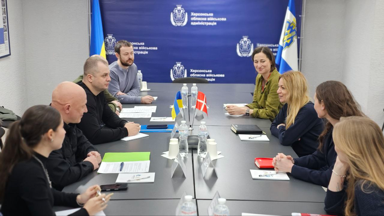 Робоча зустріч представників Херсонської ОВА та делегації з Данії. Учасники обговорюють питання співпраці за столом переговорів у залі з офіційною символікою та державними прапорами обох країн.