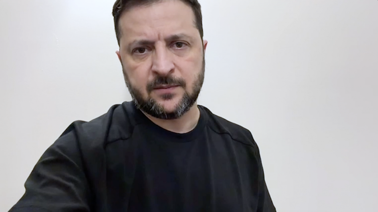 Портрет чоловіка із середньою довжиною волосся та доглянутою бородою. Він одягнений у чорну футболку та дивиться прямо в камеру на фоні світлої стіни.