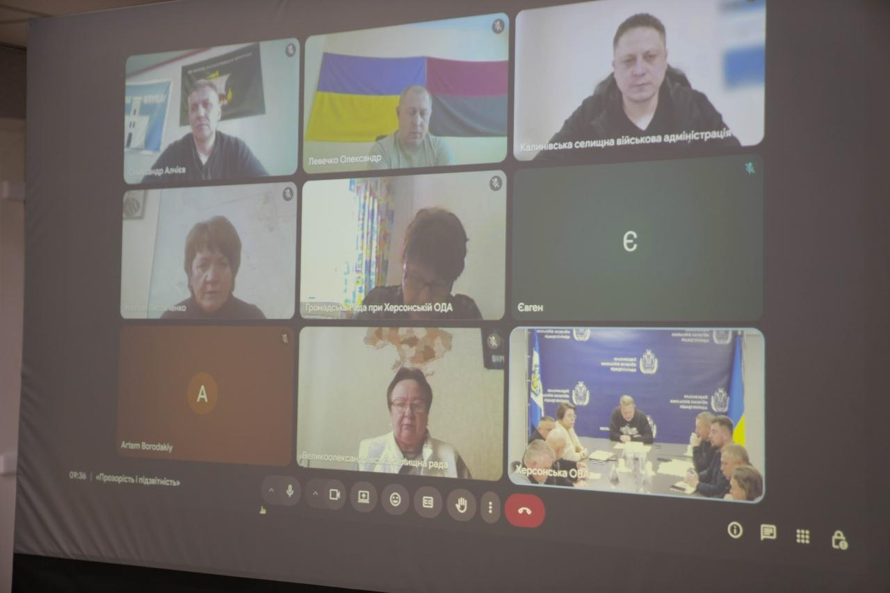 Скриншот робочої відеоконференції в Google Meet на великому проєкційному екрані. У дев'яти вікнах учасників видно людей у робочих кабінетах, державну символіку та учасників за столом нарад.