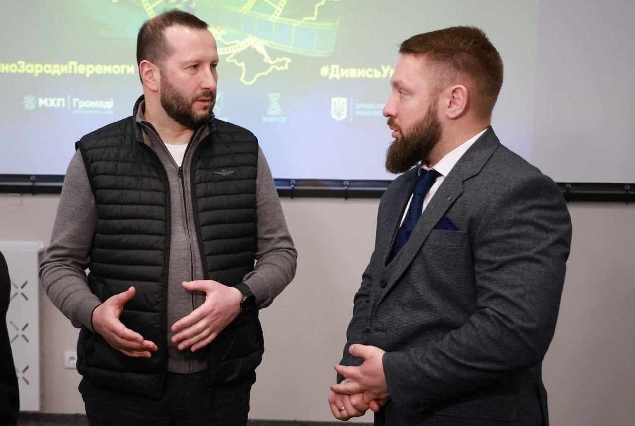 Двоє чоловіків спілкуються під час офіційного заходу. На фоні — проєкційний екран із логотипами партнерів, зокрема «МХП-Громаді», та хештегами #КіноЗарадиПеремоги і #ДивисьУкраїнське.