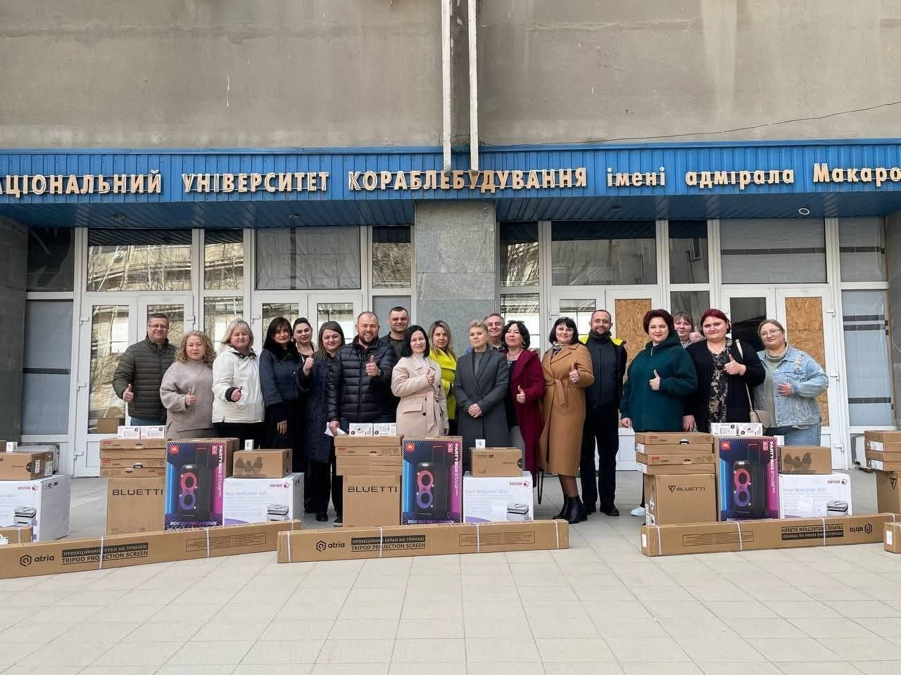 Група людей на фоні НУК імені адмірала Макарова поруч із отриманою гуманітарною допомогою: зарядними станціями та проєкційним обладнанням.