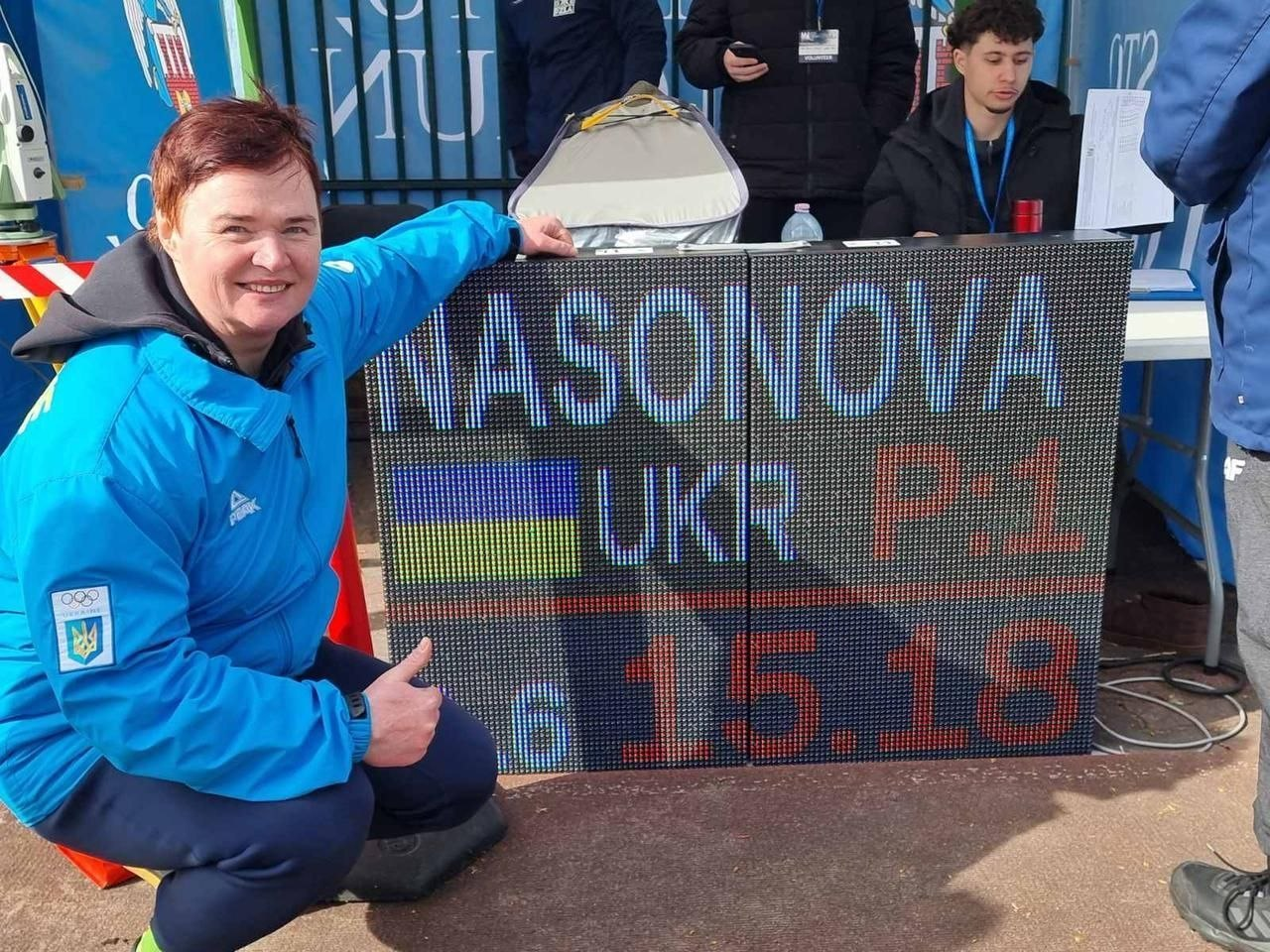 Спортсменка в блакитній формі збірної України з олімпійською символікою сидить поруч із електронним табло, на якому відображено прізвище, прапор України та результат змагань.