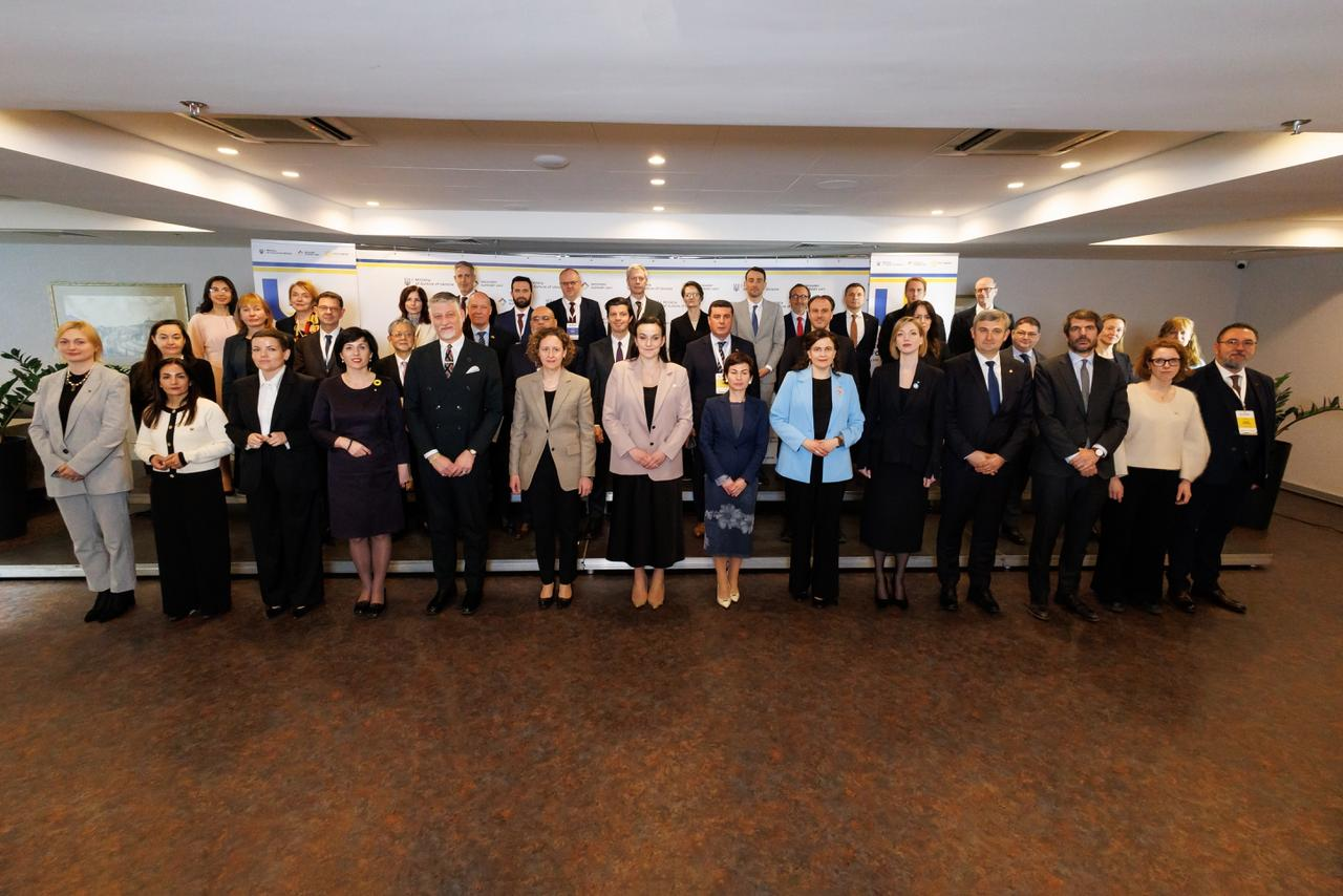 Групове фото великої кількості людей в офіційному вбранні (костюмах та сукнях), які стоять у кілька рядів у приміщенні на фоні банерів.