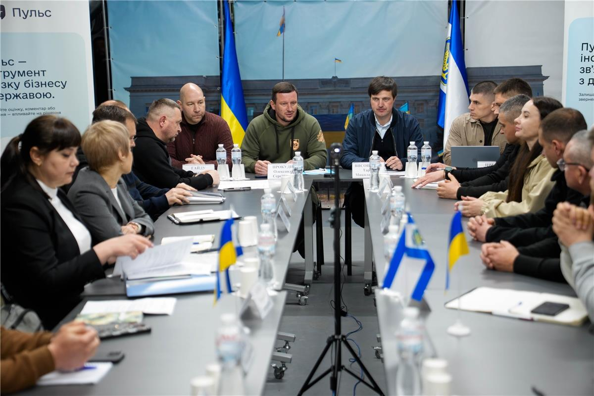 Робоча зустріч представників влади та бізнесу за великим круглим столом. Учасники обговорюють документи; на столі розміщені прапорці України та пляшки з водою. На фоні — банери з інформацією про платформу «Пульс» та зображенням офіційної будівлі.