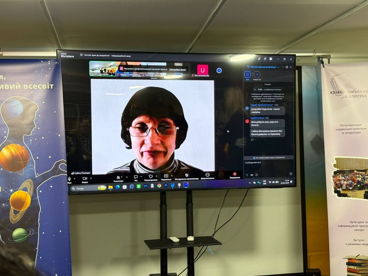 Великий телеекран у бібліотеці, на якому транслюється онлайн-зустріч у Zoom зі спікеркою та відкритим чатом. Поруч розташовано плакат із планетами та банер книгозбірні.