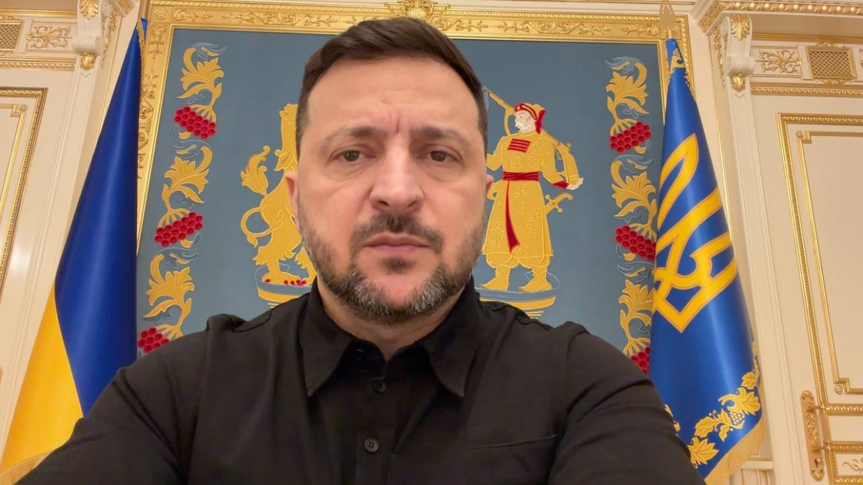 Чоловік з короткою бородою та в чорній сорочці стоїть на фоні державних символів України та офіційного інтер’єру.