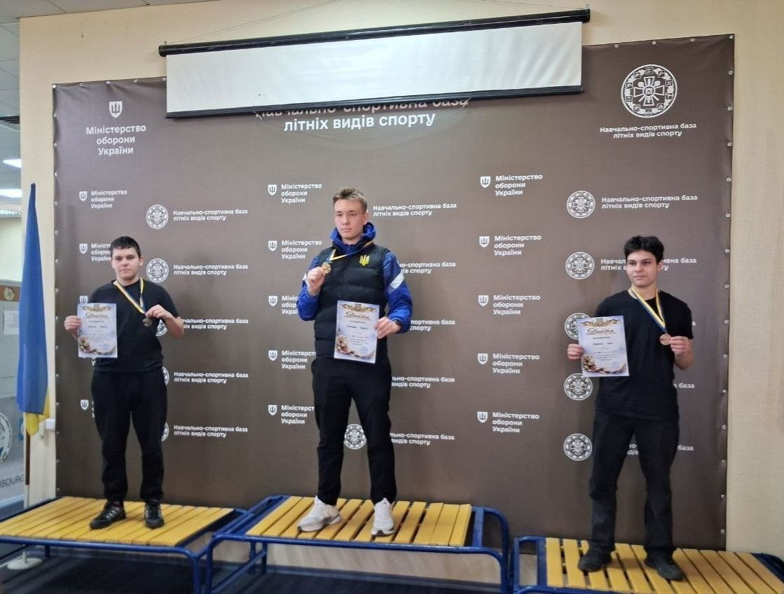 Три призери спортивних змагань на п'єдесталі з медалями та грамотами. На фоні — банер Навчально-спортивної бази літніх видів спорту Міністерства оборони України та державний прапор.