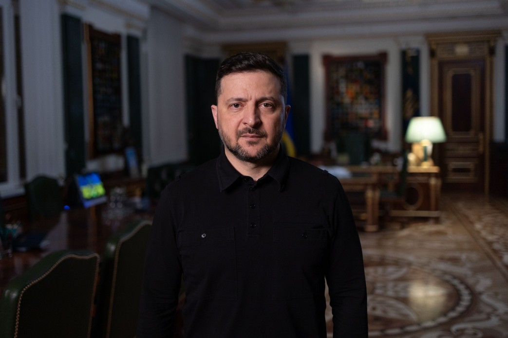 Чоловік з короткою бородою та зачіскою у чорній сорочці поло стоїть у центрі офісного приміщення з класичним інтер'єром.