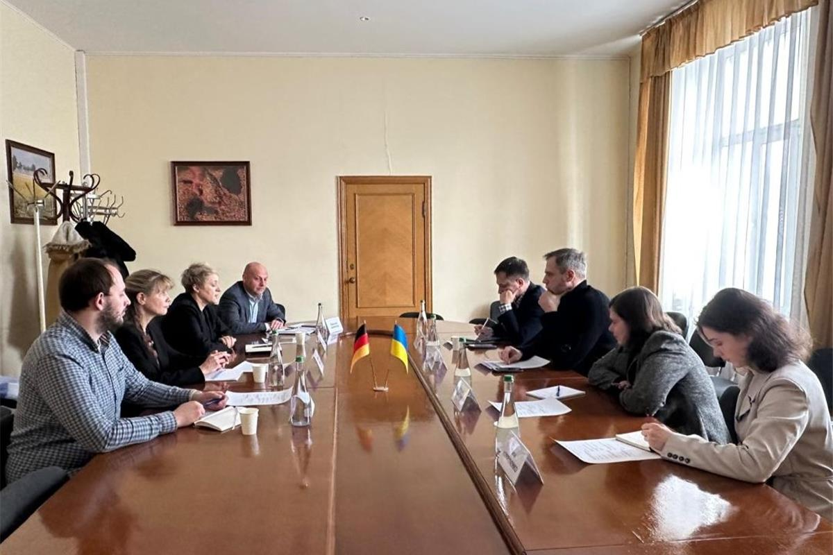 Восьмеро людей проводять офіційну зустріч за довгим столом із прапорцями України та Німеччини в кабінеті зі світлими стінами.