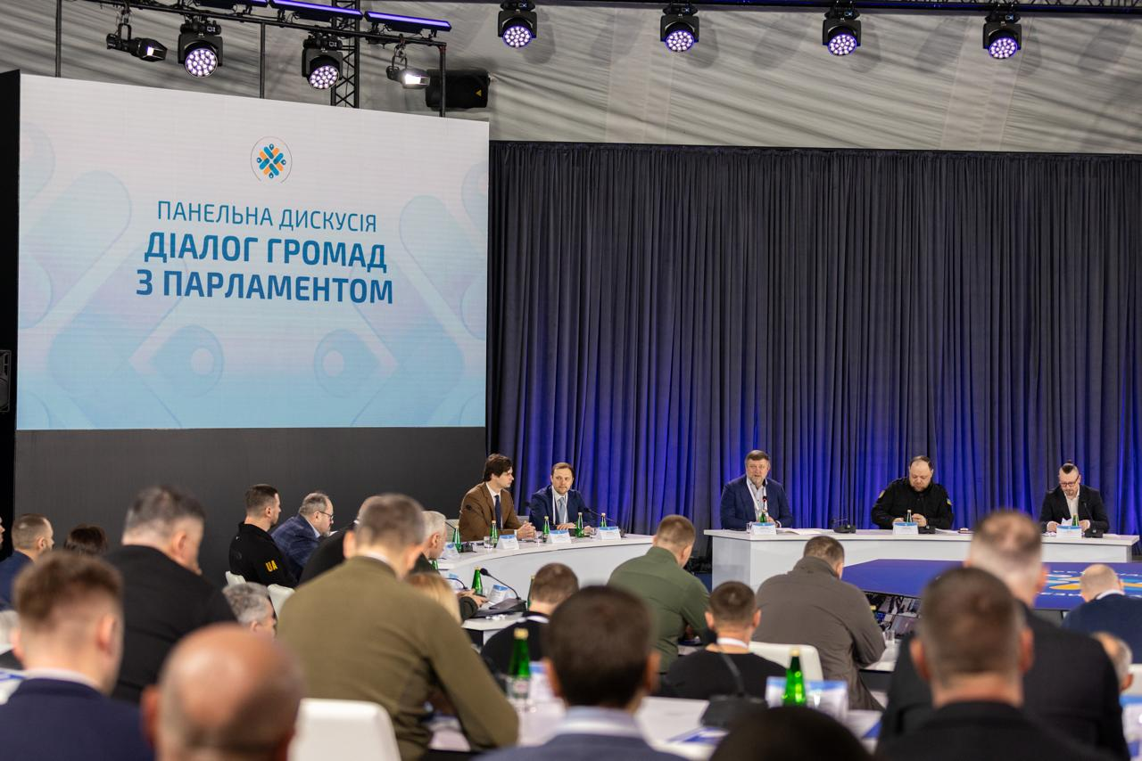 Панельна дискусія «Діалог громад з Парламентом» у великому залі. П'ятеро спікерів сидять за столом перед аудиторією на фоні великого екрана з назвою заходу та синіх штор.