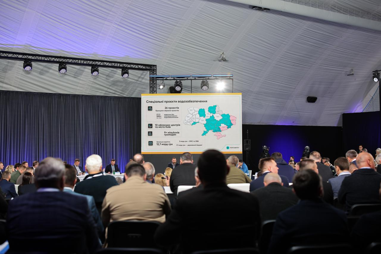 Вид із залу на численну аудиторію під час офіційного форуму. На великому екрані представлена презентація «Спеціальні проєкти водозабезпечення» з мапою України, де виділено пріоритетні області, та статистичними даними.