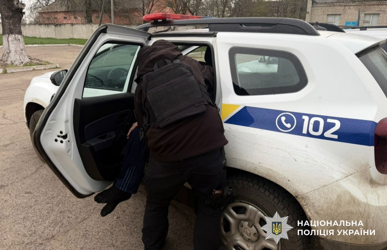Працівник поліції допомагає людині сісти в службовий автомобіль. У куті — логотип Національної поліції України.