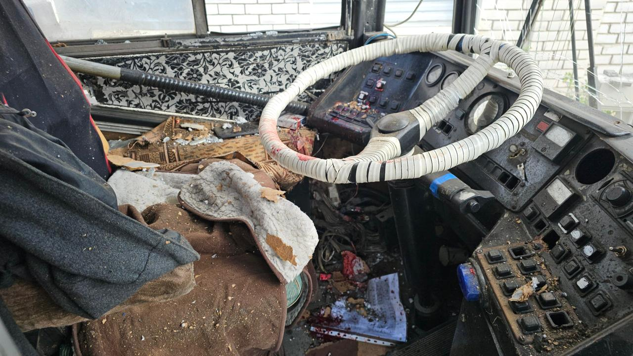 Занедбана кабіна водія тролейбуса: кермо в білій обмотці, приладова панель і безлад на сидінні зі сміттям та уламками.