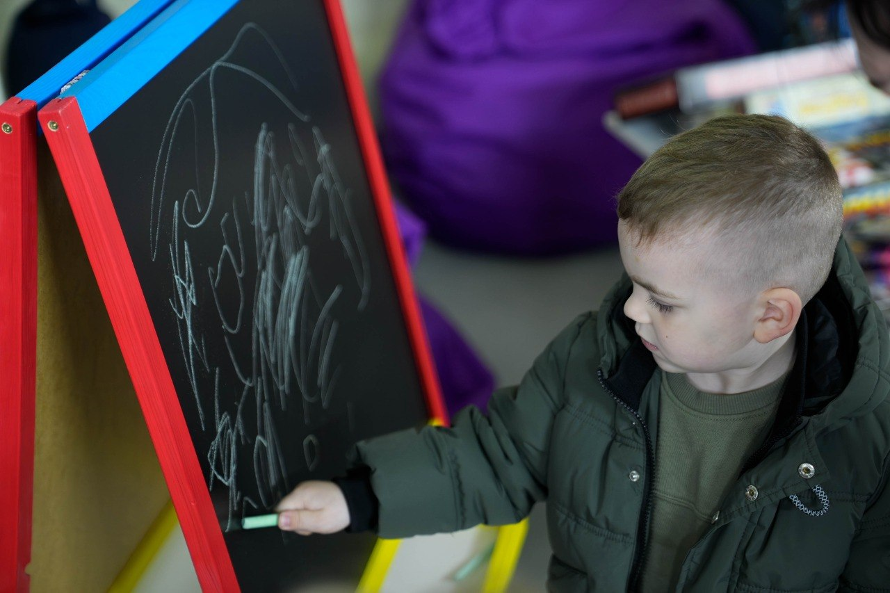 Хлопчик малює крейдою на дошці в червоній рамці в ігровій кімнаті.