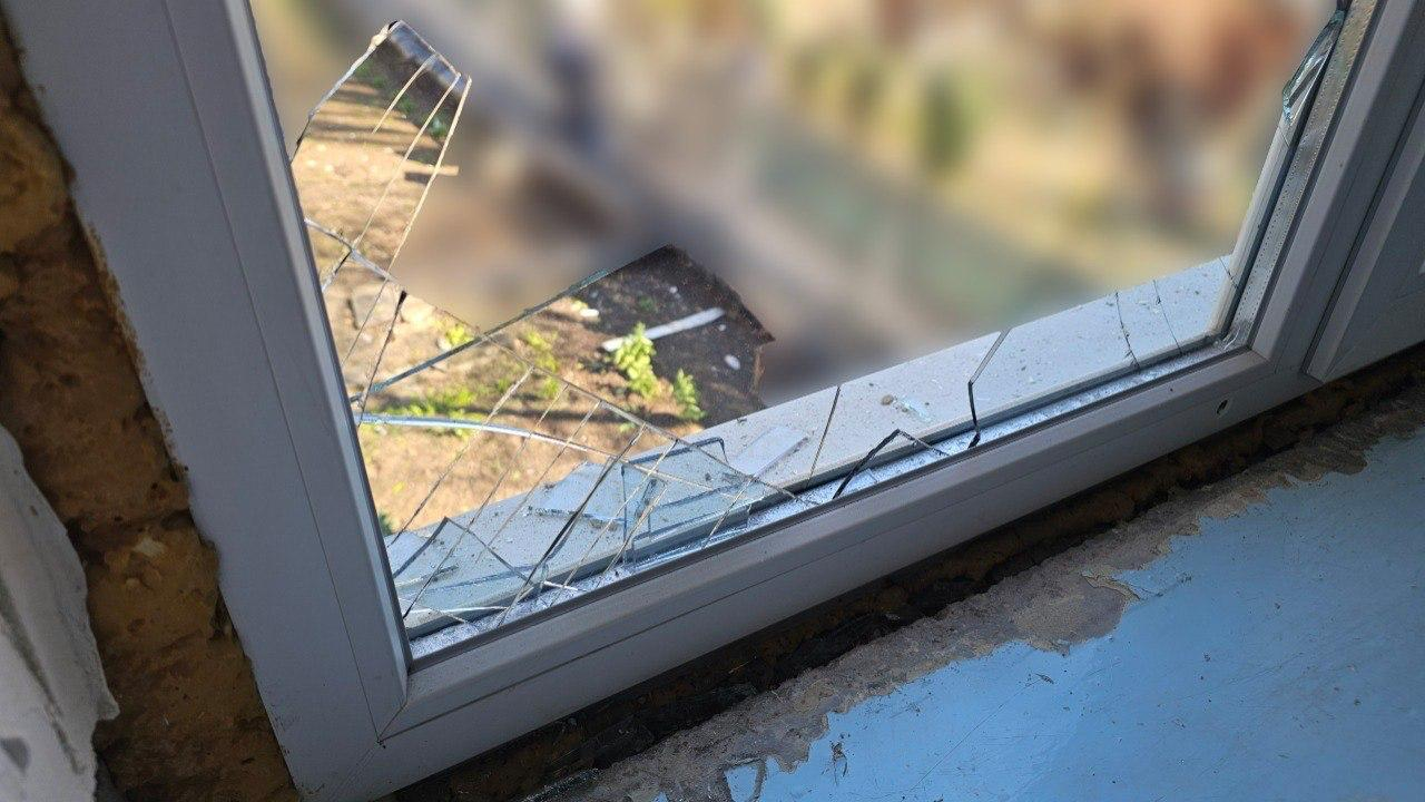 Розбите вікно в білій рамі, через яке видно вулицю. На підвіконні та в рамі залишилися гострі уламки скла.