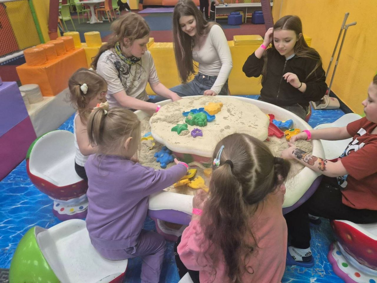 Група дітей та підлітків грається з кінетичним піском за круглим столом у дитячій ігровій зоні.