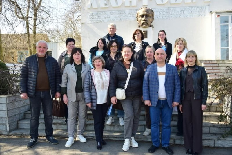 Група людей стоїть на сходах біля пам'ятника-погруддя Тарасу Шевченку. На світлій стіні за ними видно написи та частину назви установи. Подія відбувається на вулиці в сонячну погоду.