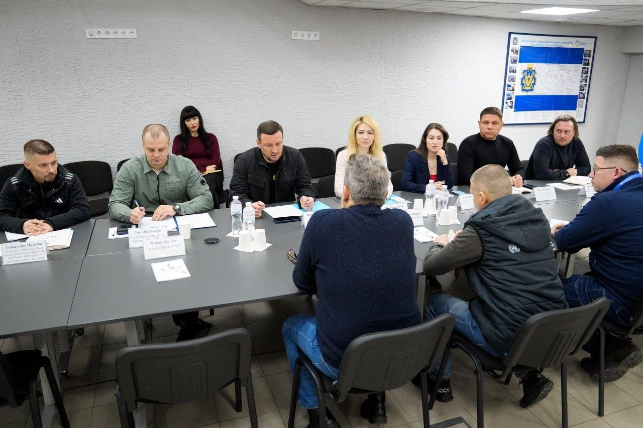 Група людей за столом під час офіційної зустрічі. На столі документи та пляшки з водою; учасники обговорюють робочі питання в офісному приміщенні.