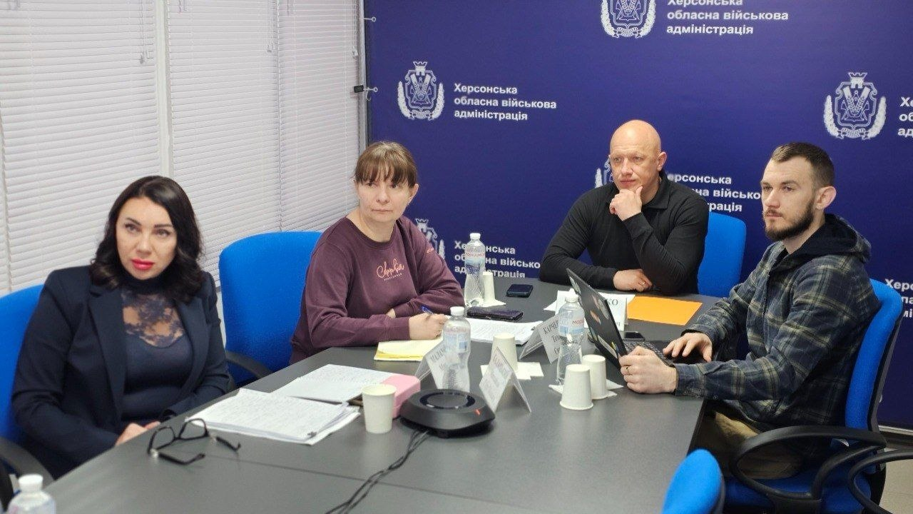 Чотири особи за столом під час робочої зустрічі в офісному приміщенні на фоні синього банеру.