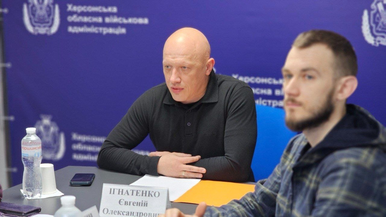 Двоє чоловіків за столом під час наради на фоні синього брендованого банера.