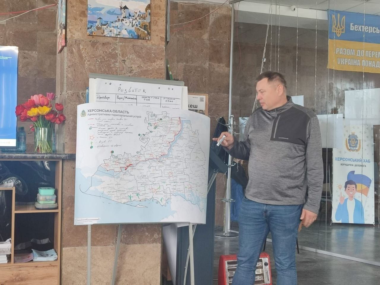 Чоловік із маркером у руках біля карти Херсонської області під час робочого обговорення в офісному приміщенні.