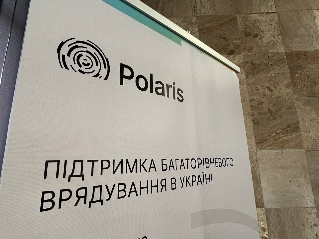 Інформаційний банер проєкту «Polaris» із написом «Підтримка багаторівневого врядування в Україні» на фоні світлої кам'яної стіни.