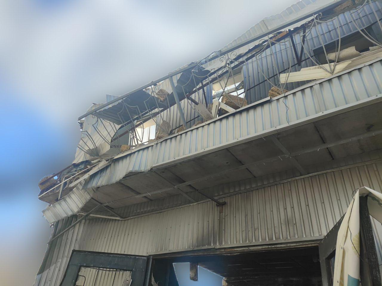Пошкоджена промислова або складська будівля з металевим облицюванням. Верхня частина споруди зруйнована, металеві листи покрівлі деформовані та звисають донизу.