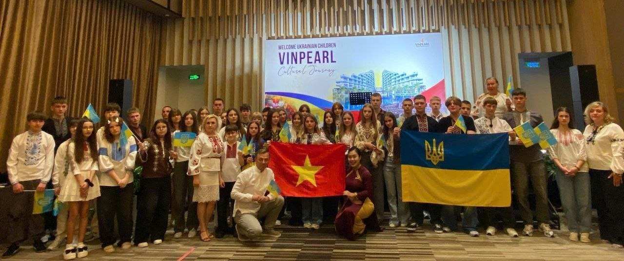 Група молодих людей та дорослих, багато з яких у вишиванках, позують для спільного фото в залі. У центрі вони тримають прапори України та В’єтнаму. На фоні видно банер із написом «Welcome Ukrainian Children Vinpearl Cultural Journey».