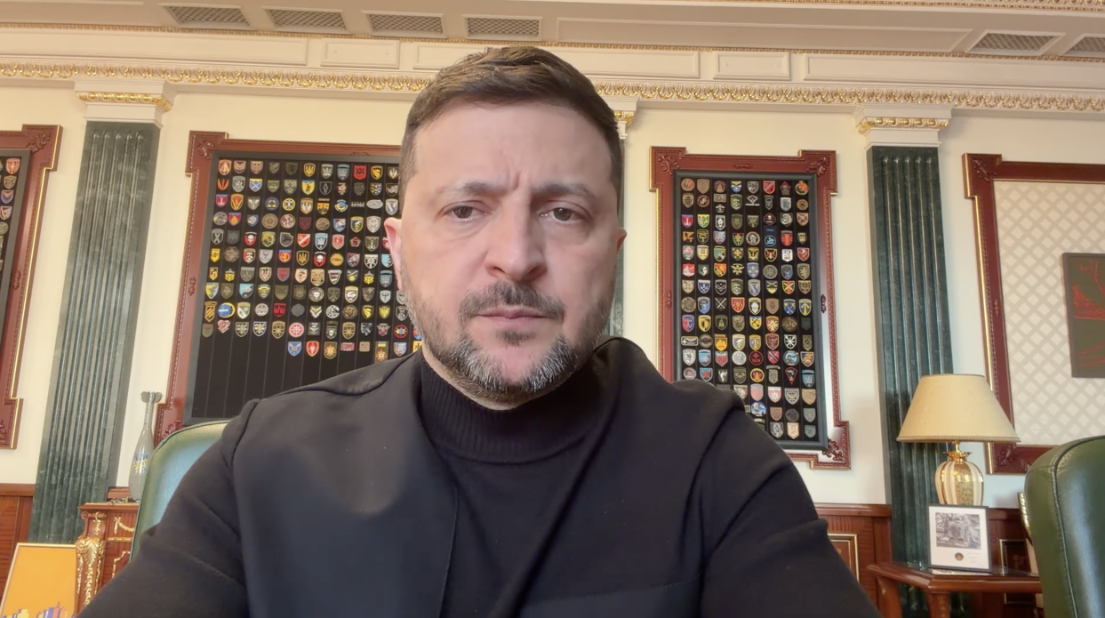 Чоловік у темному одязі на фоні стіни з колекцією військових шевронів.
