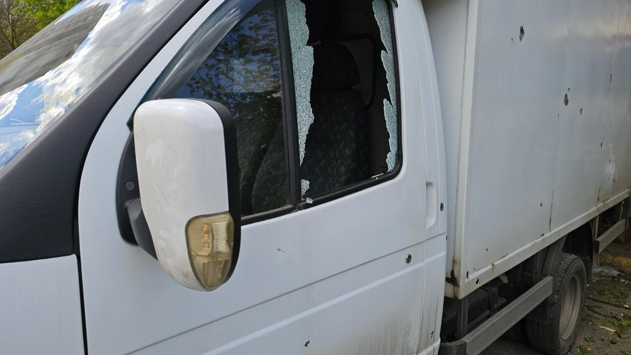 Білий вантажний автомобіль із розбитим боковим склом з боку пасажира. На дверцятах та фургоні машини помітні дрібні пошкодження, схожі на сліди від уламків.