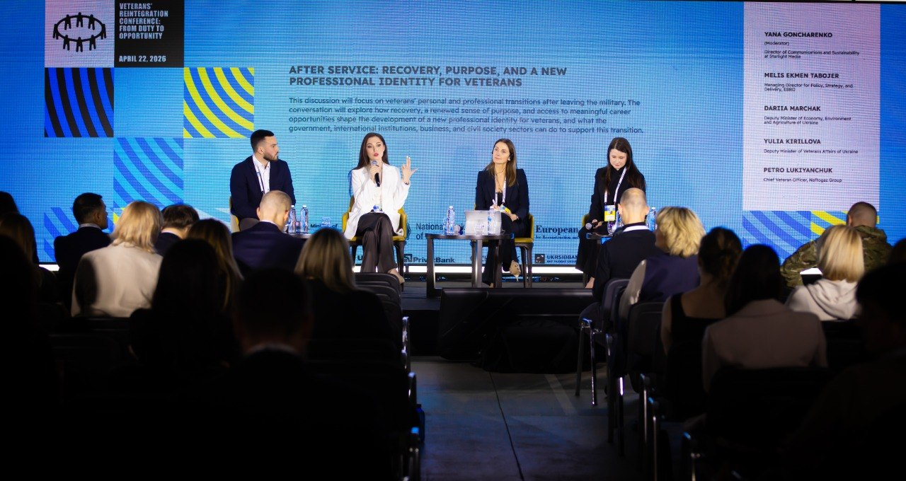 Панельна дискусія на тему адаптації ветеранів після служби. Чотири спікери сидять на сцені перед великим екраном із заголовком «AFTER SERVICE: RECOVERY, PURPOSE, AND A NEW PROFESSIONAL IDENTITY FOR VETERANS». У залі знаходяться слухачі.