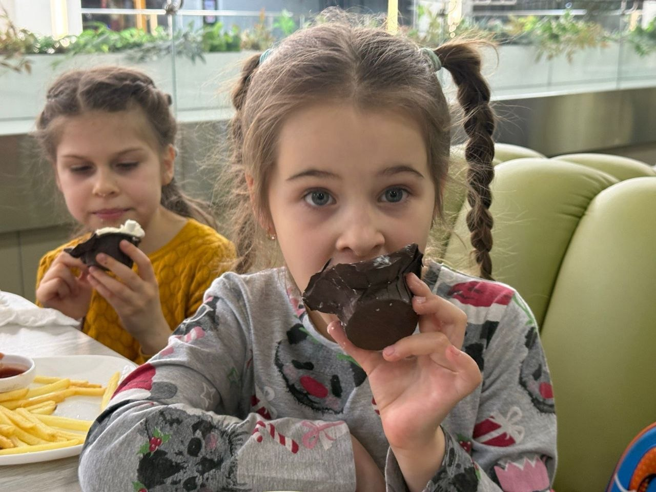 Дві дівчинки сидять за столом у кафе та їдять шоколадні десерти. Поруч на столі стоїть тарілка з картоплею фрі.