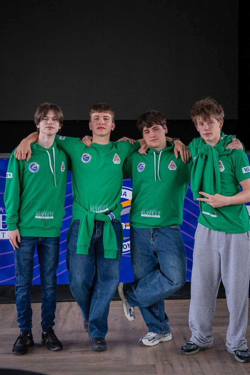Четверо хлопців у зелених худі та футболках із логотипами «The Howard G. Buffett Foundation» стоять обнявшись на фоні сцени. Вони позують перед синім брендованим банером у приміщенні.