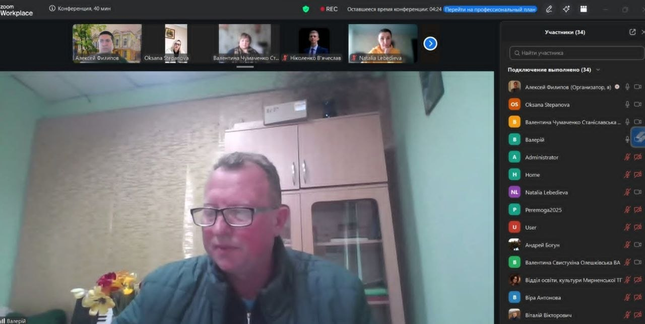 Скриншот вікна онлайн-конференції, на якому в центрі зображений чоловік в окулярах під час виступу на фоні кімнатного інтер’єру. У верхній частині екрана відображаються мініатюри інших учасників, а праворуч — бічна панель зі списком присутніх.