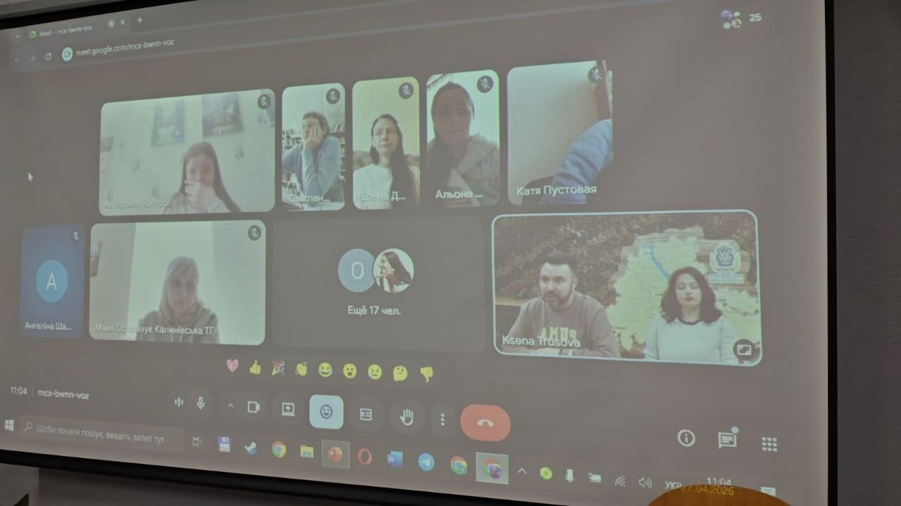 Проєкція вікна відеоконференції Google Meet на великий екран. На екрані видно плитку з багатьма учасниками зустрічі, панель інструментів керування дзвінком та інтерфейс робочого столу комп'ютера.