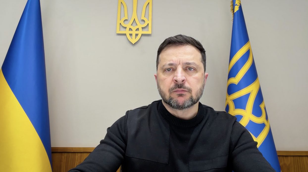 Офіційне відеозвернення посадової особи на фоні державних символів України. У кадрі — чоловік у темному одязі, позаду якого розміщено Державний Герб та два прапори: національний синьо-жовтий і штандарт Президента.