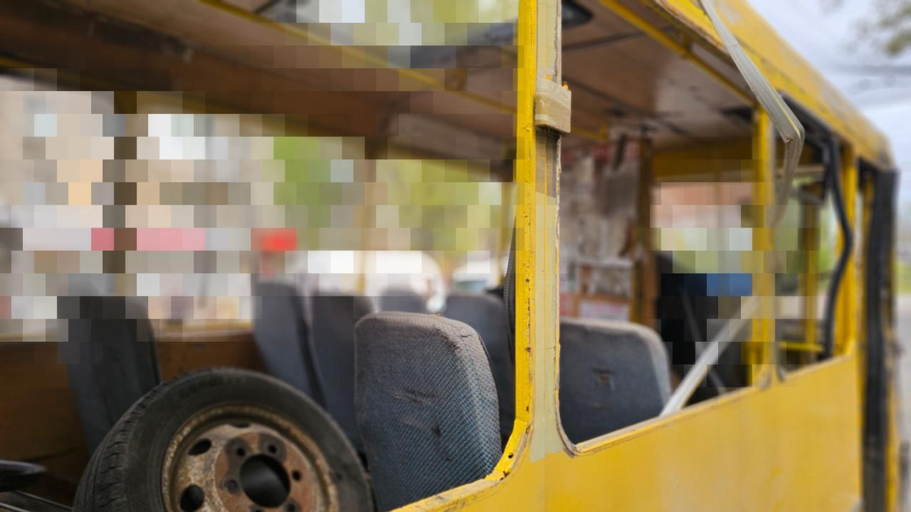 Салон пошкодженого жовтого автобуса без вікон, де всередині лежить запасне колесо. Частина зображення прихована пікселями.