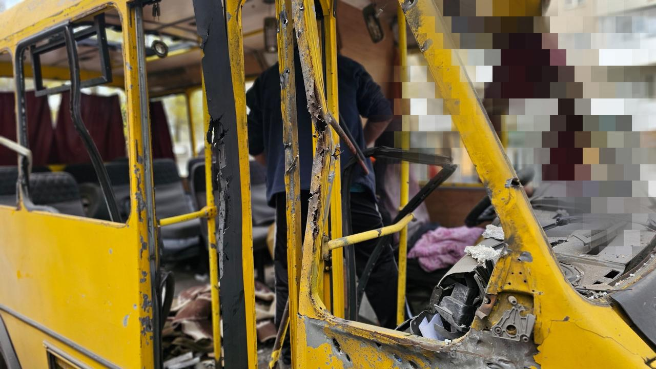 Жовтий автобус із серйозними пошкодженнями кузова, розбитими вікнами та слідами від уламків. Через відсутні двері та вікна видно понівечений салон, а край зображення праворуч частково прихований пікселями.